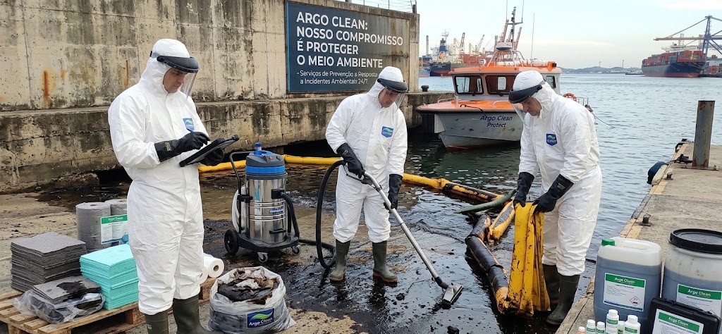 Equipe da Argo Clean em traje de proteção realizando descontaminação de material oleoso junto a uma barreira de contenção